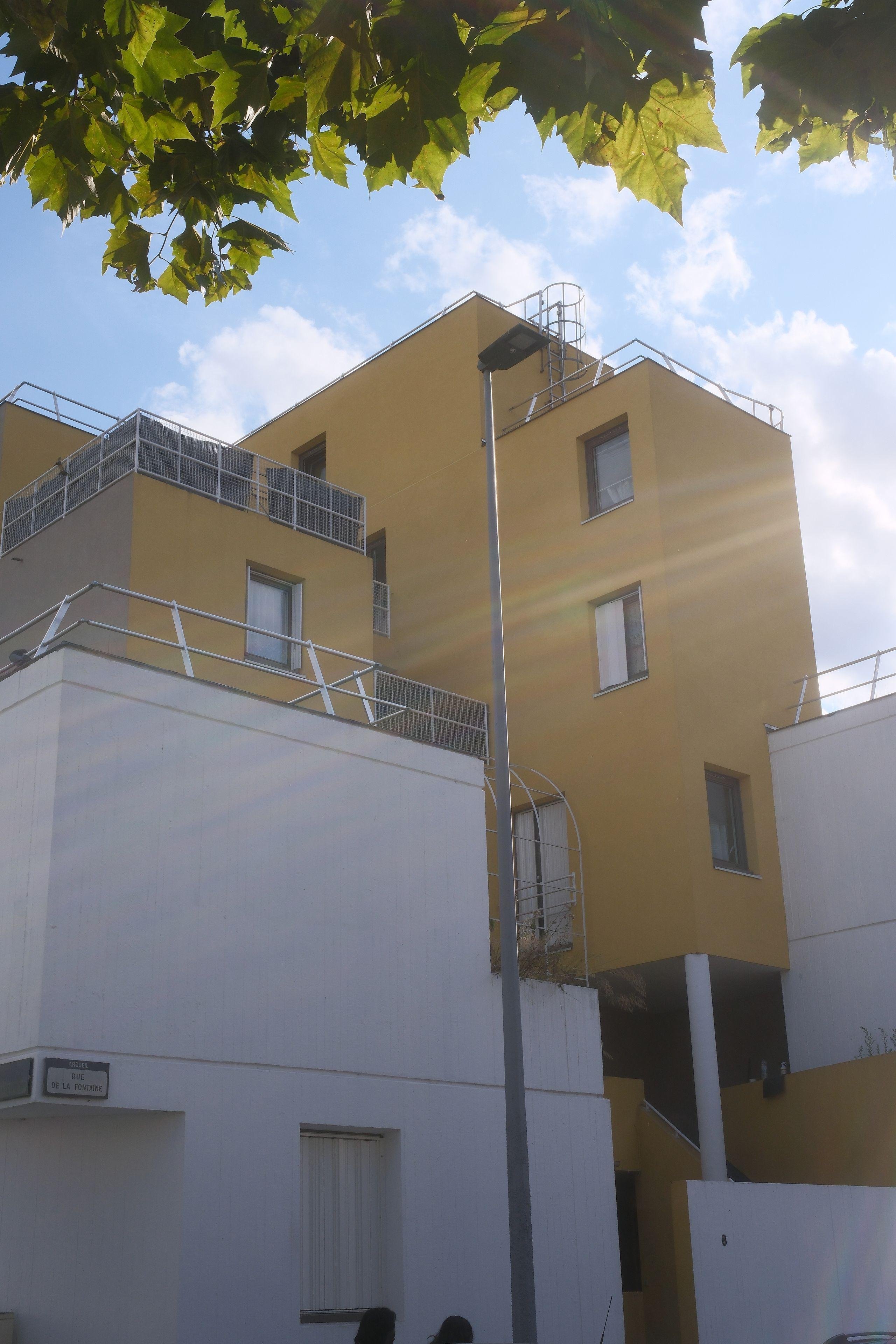 Photo verticale. Un immeuble très irrégulier fait de formes cubiques comme mis au hasard. Ceux du 1er plan en blanc, et puis en jaune pour ceux plus en dedans