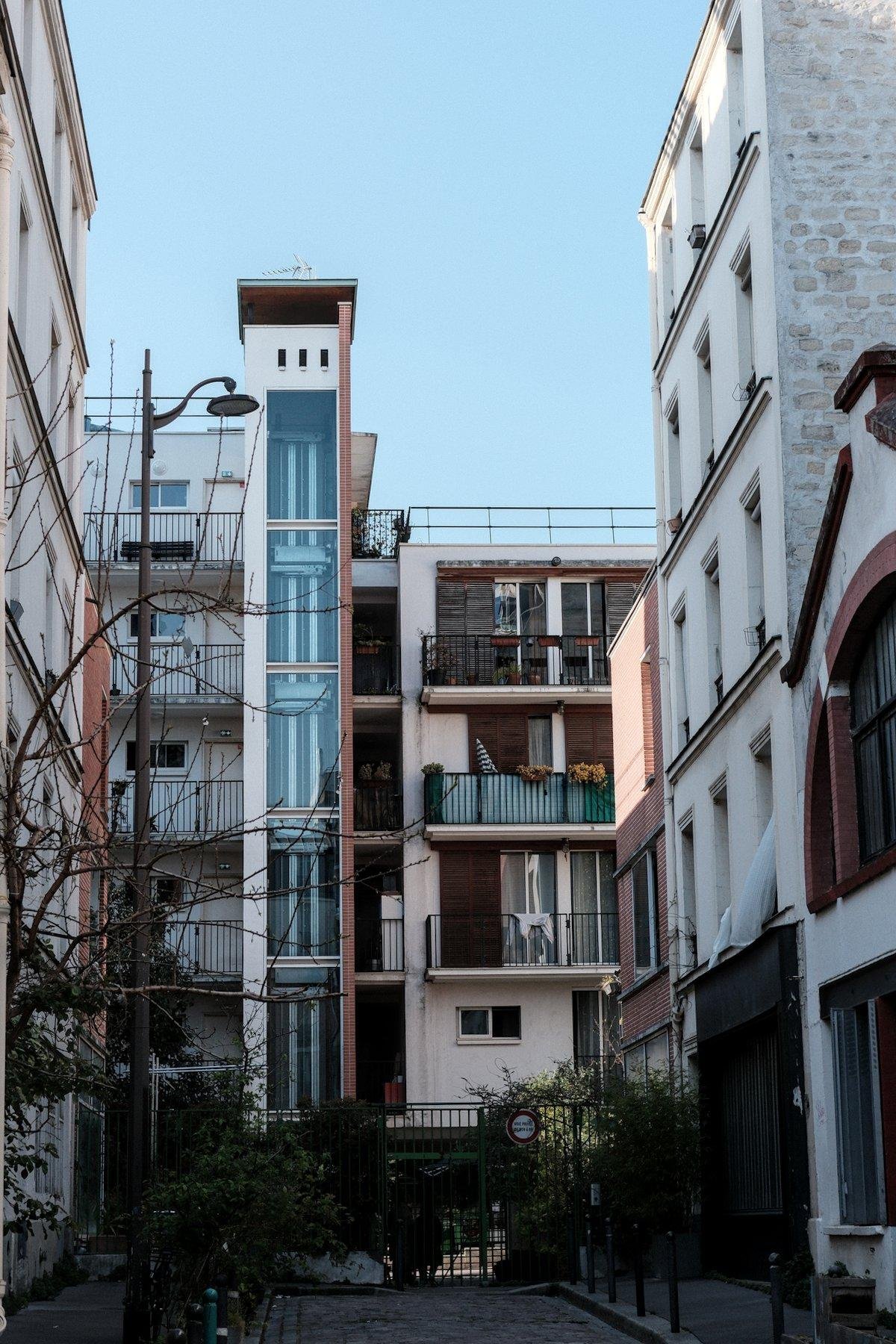 Photo verticale. Un immeuble au fond d’une impasse dont la cage d’ascenseur est vitré
