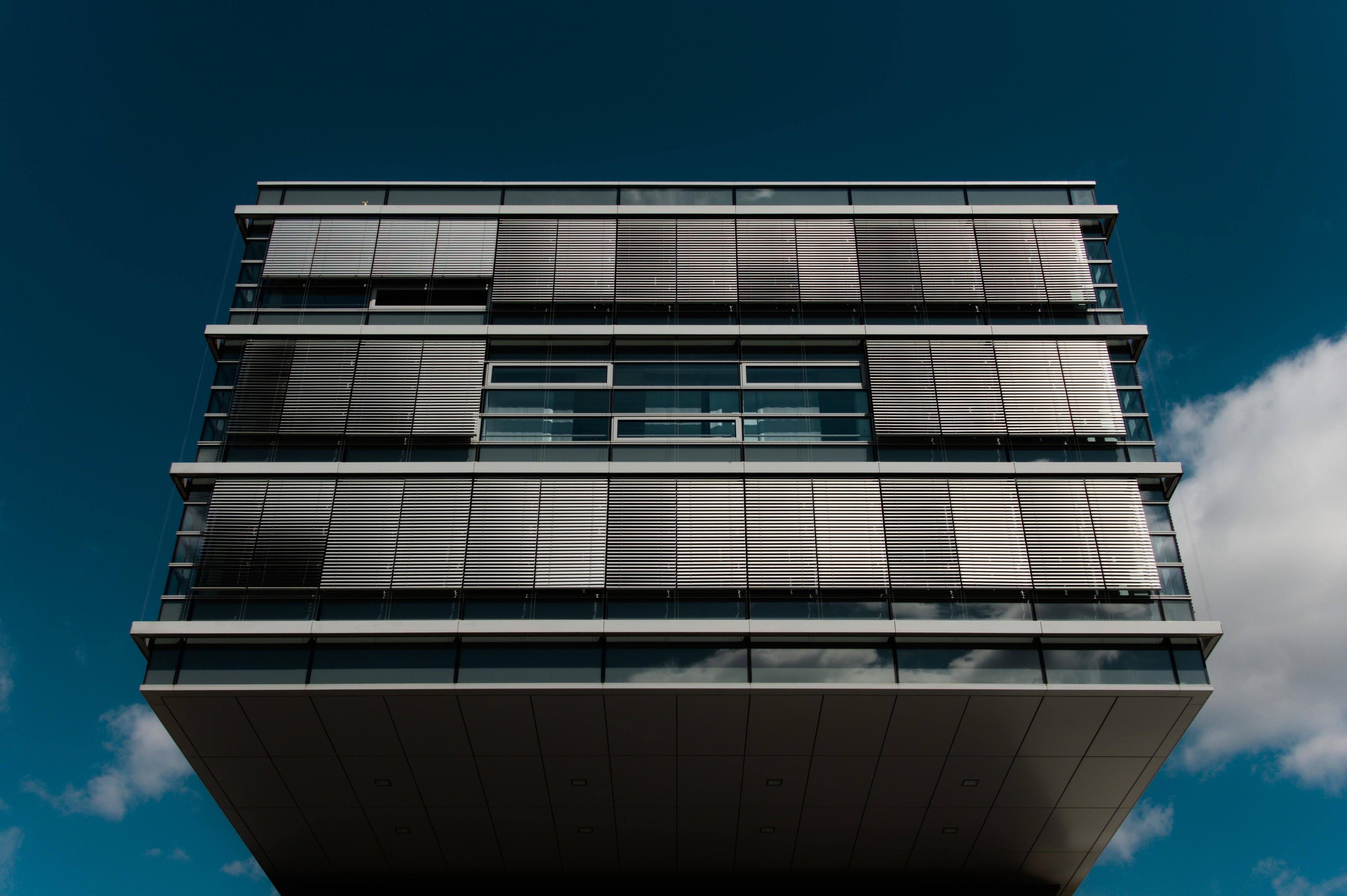 Low-angle view of a modern glass-and-metal building with horizontal window bands and exterior louvered sunshades, framed against a dark blue sky with a few clouds.