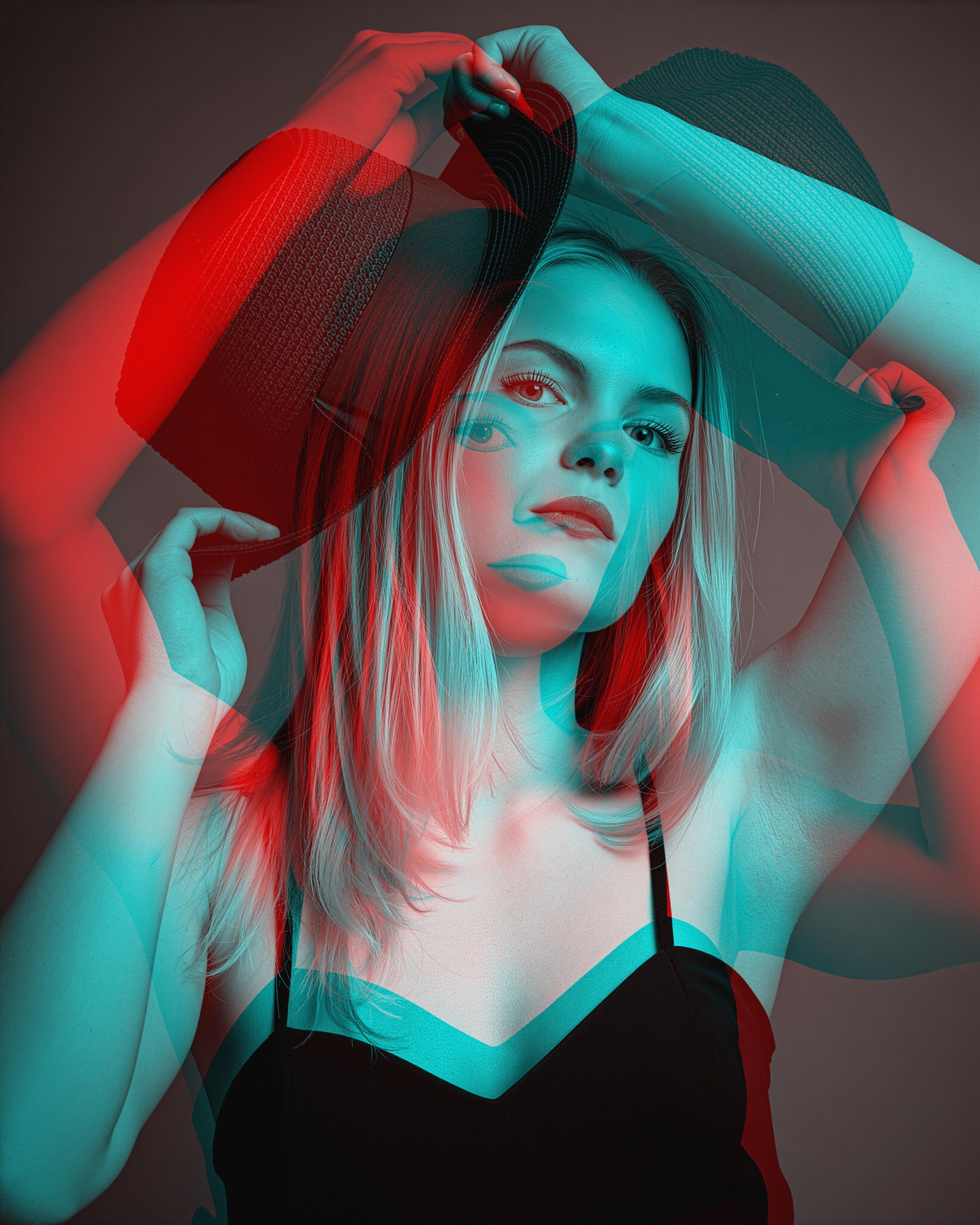 Woman with long hair wearing a black top and a hat, captured in a double exposure effect. Red and blue overlays create a layered visual, with one hand adjusting the hat. Neutral gray background enhances the color contrast in the composition.