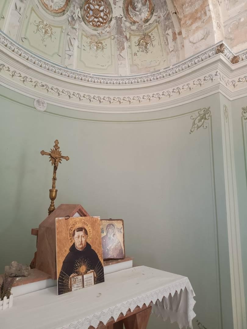 Immagini sacre, raffiguranti San Tommaso e la Madonna col Bambino, poggiate su un altarino, con un crocifisso in secondo piano. Lo sfondo è intonacato, verde molto leggero.